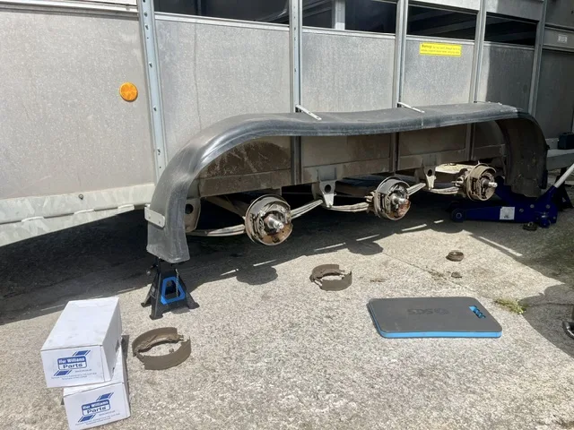 Twin-axle commercial trailer up on stands with the wheels off, hubs and brake shoes exposed mid-service