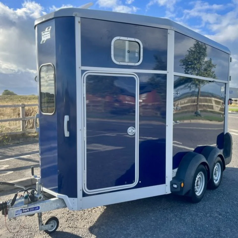 Navy blue Ifor Williams HB511 twin-axle horse trailer parked on a road, available for hire from Peak Trailers